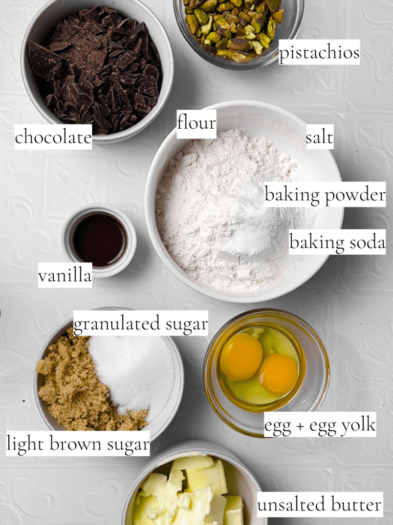 Ingredients you will need for the pistachio dark chocolate chunk cookies. Includes pistachios, dark chocolate, flour, salt, baking powder, baking soda, vanilla, granulated sugar, light brown sugar, egg, egg yolk, and unsalted butter.