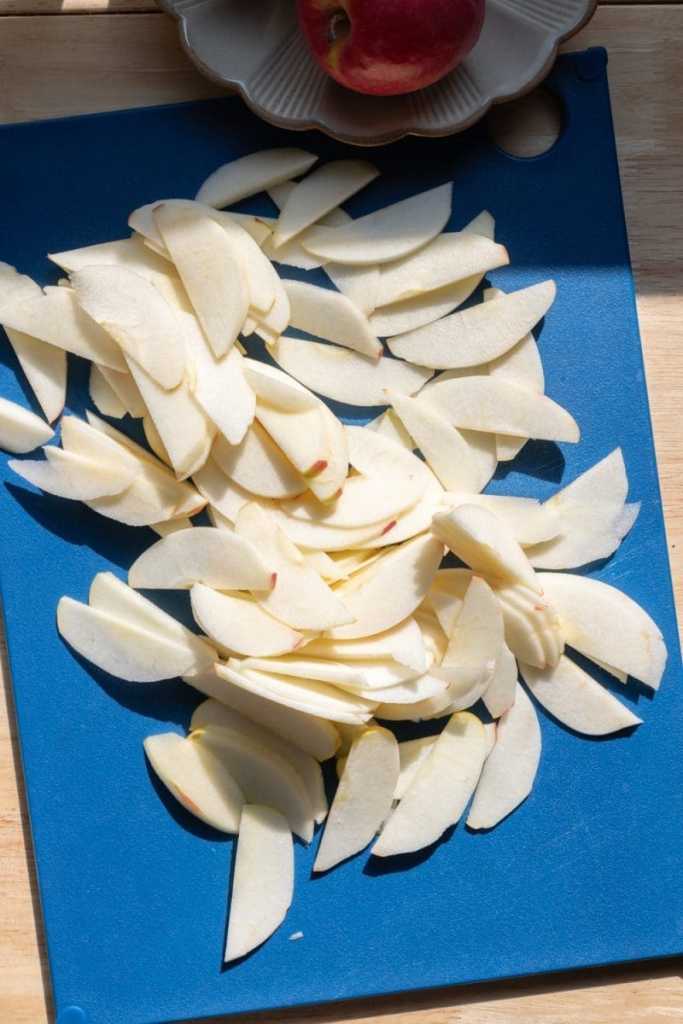 Apples sliced thinly on a cutting board.