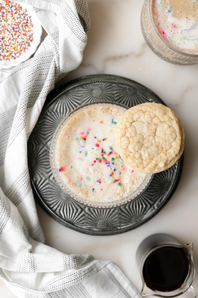 a flat lay of the sugar cookie latte, with colorful sprinkles and a sugar cookie on top of it.
