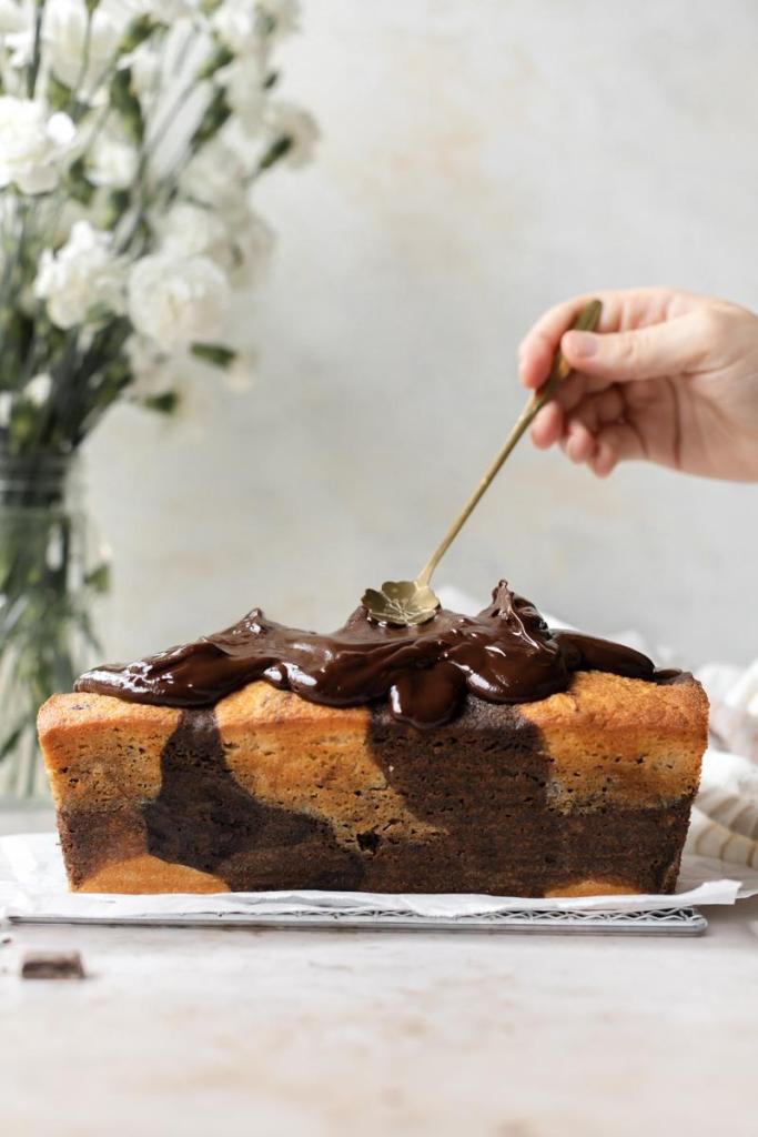 spreading the ganache over the loaf cake with a gold floral spoon
