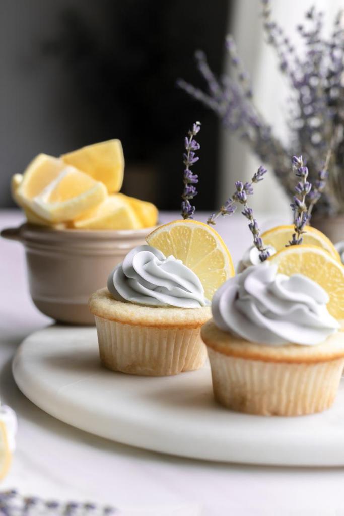 a close up of the lemon lavender cupcakes, with a bowl of lemons and vase of lavender behind them