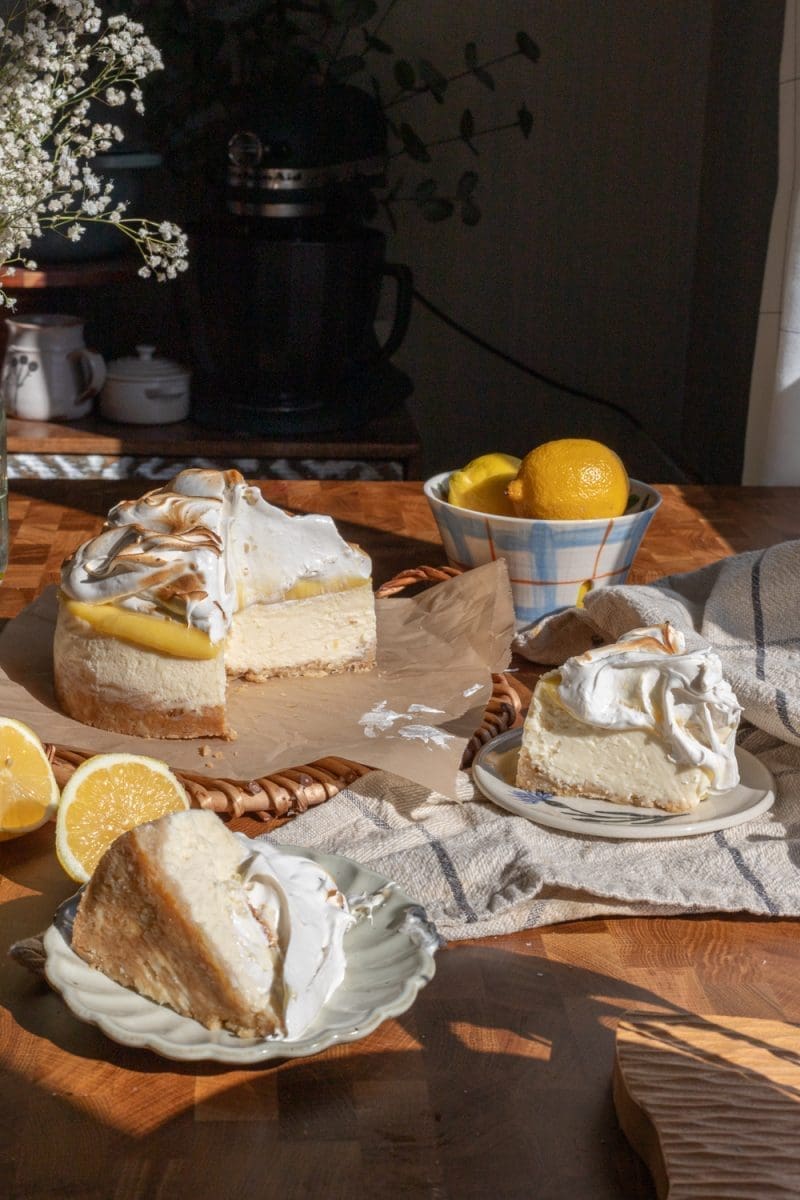 The sliced lemon meringue cheesecake with two plated slices of cheesecake in front of it.