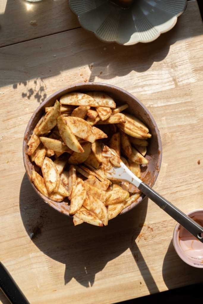 The sliced apples mixed with salted caramel in a mixing bowl.