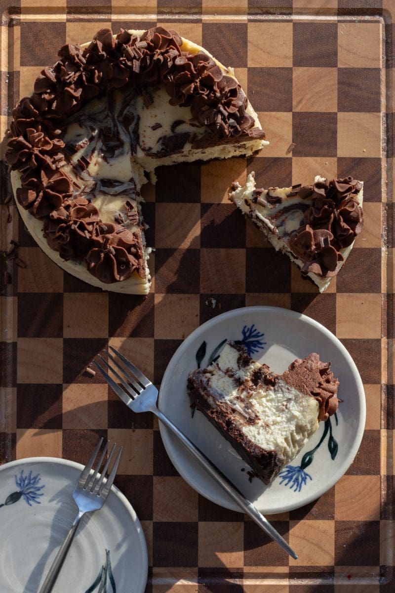Brownie cheesecake stylized on a serving platter, with a slice of the cheesecake on a plate next to it.