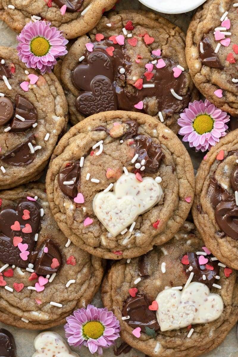 Flat lay of the valentine's day chocolate chip cookies stacked on top of each other, surrounded by purple flowers