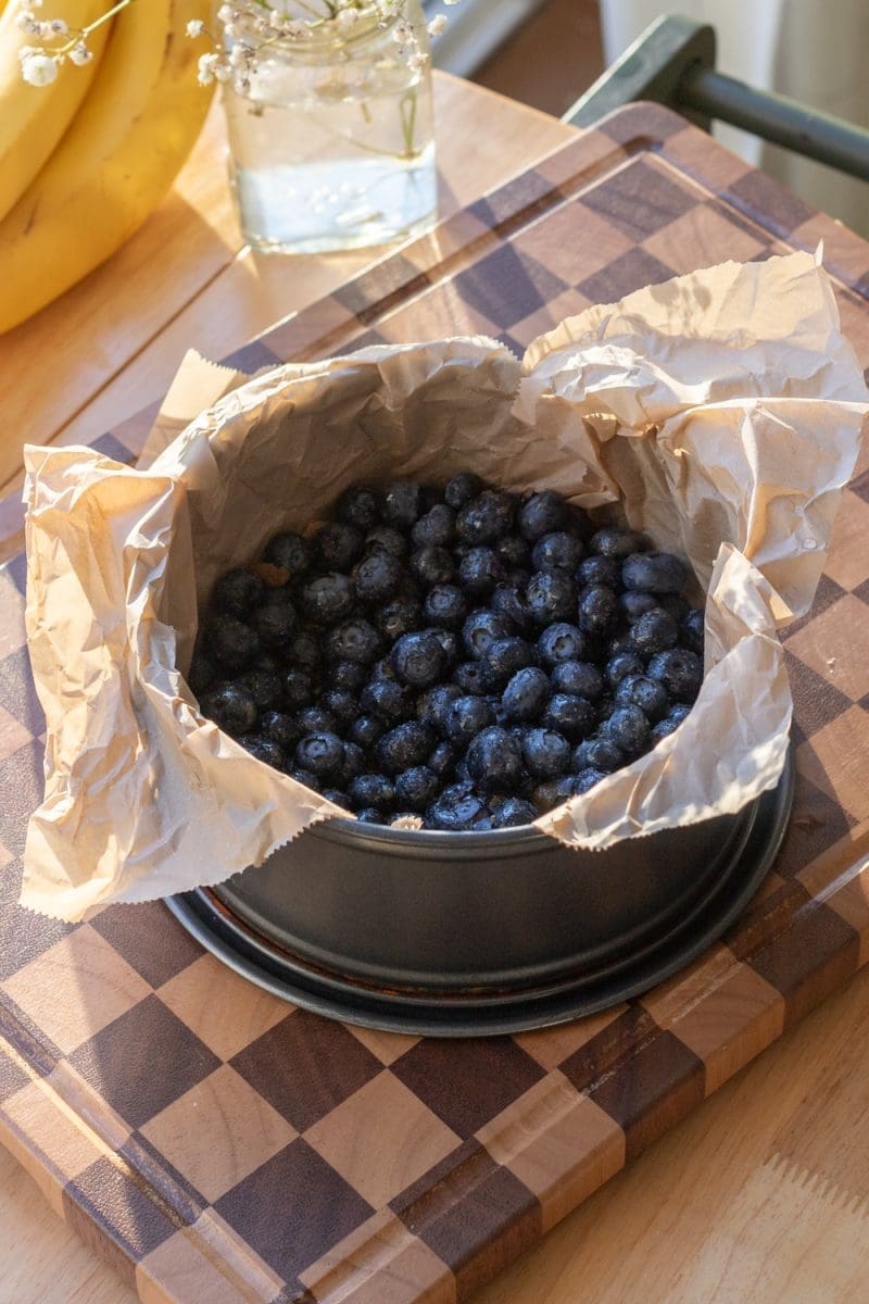 The blueberries at the bottom of a lined springform pan.