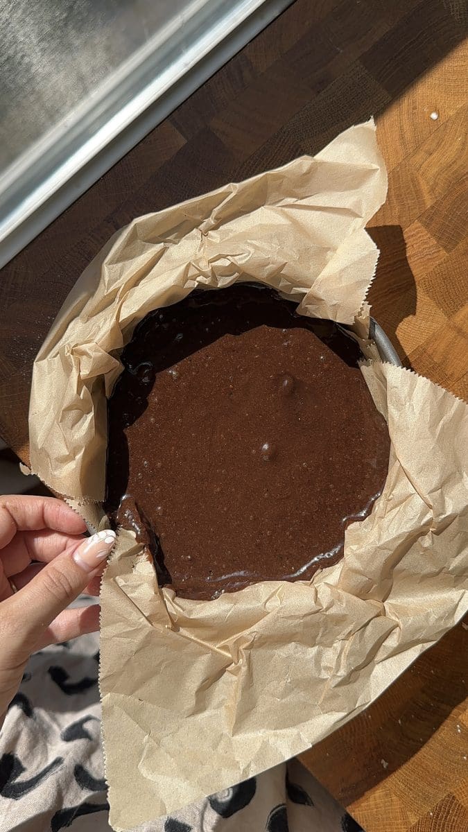 The chocolate cake batter in a lined 6" pan.