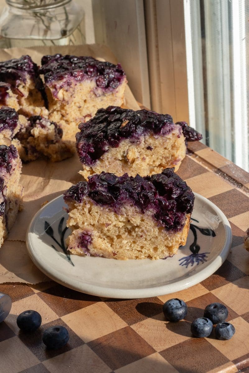Slice of banana blueberry upside down cake on a plate next to the whole cake.
