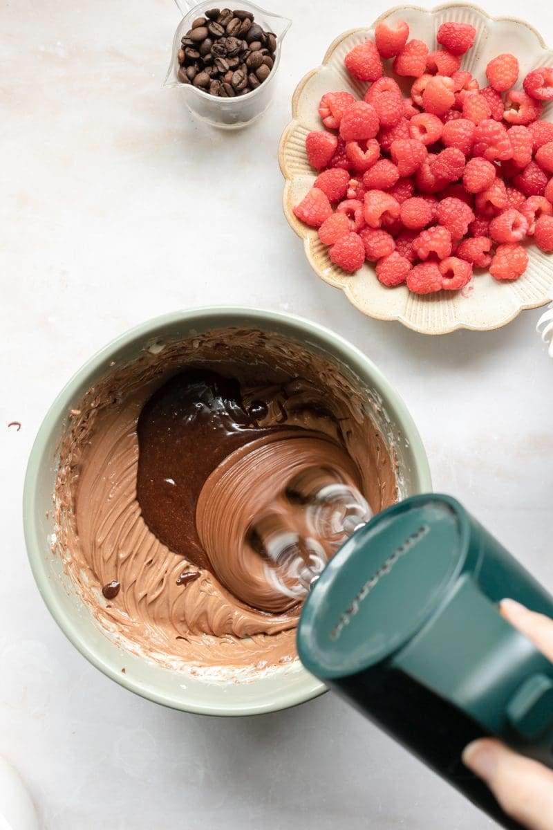 Hand mixer beating dollops of chocolate pudding into the butter mixture.