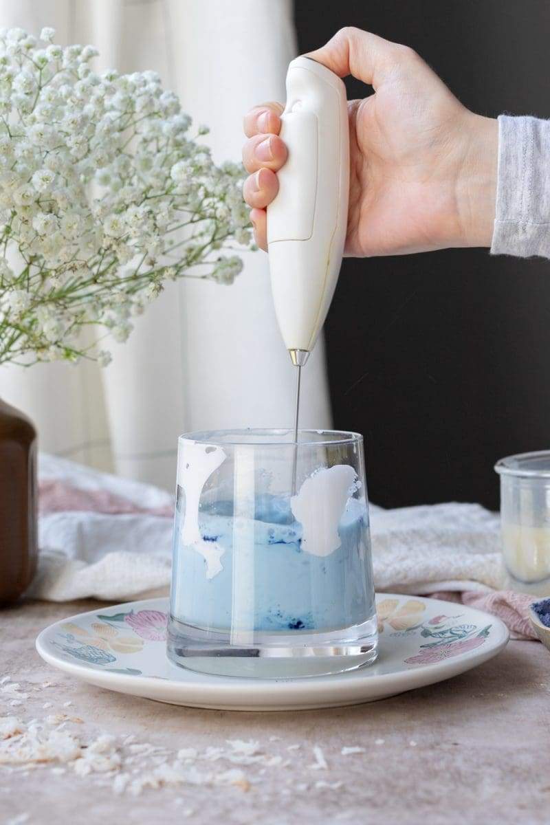 Mixing together the milk, butterfly pea powder and coconut sauce with an electric frother