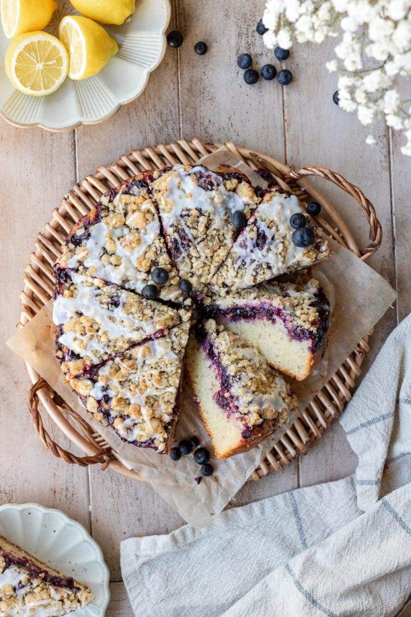 Stylized flat lay of the whole lemon blueberry crumb cake on a tray, with two slices facing up towards the camera to show the cross-section