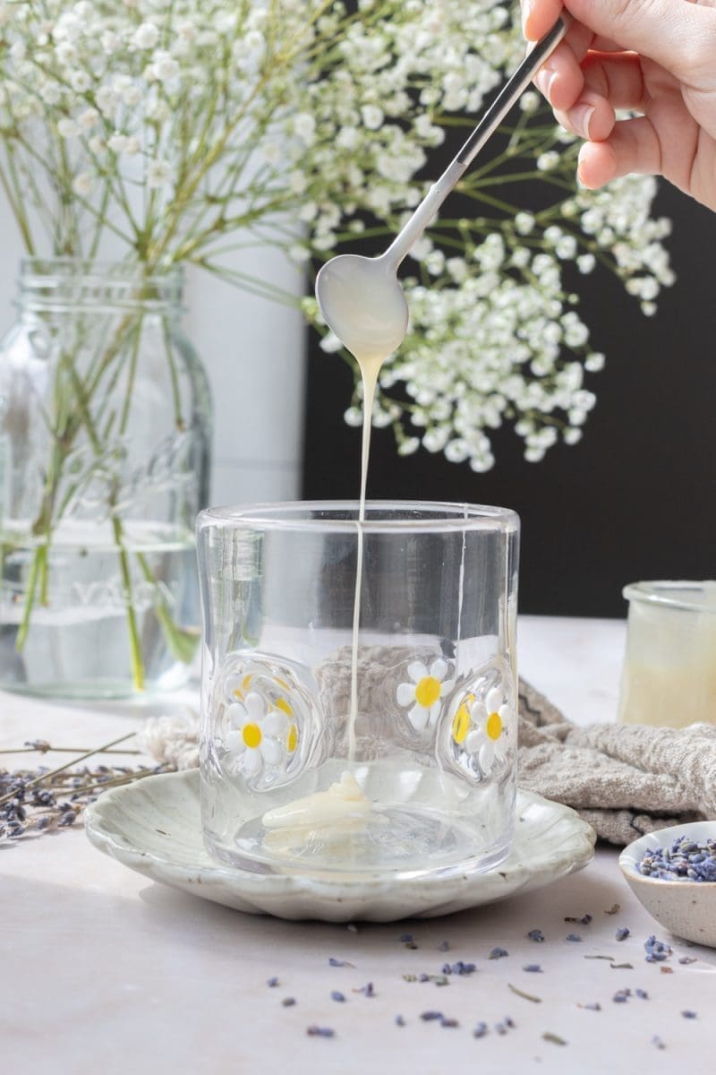 A spoon drizzling white chocolate lavender sauce into a cup.