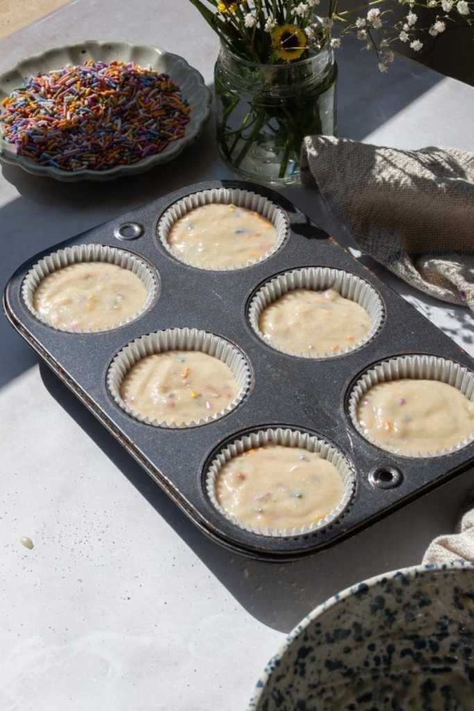 The cupcake batter distributed between six parchment liners in a cupcake pan.
