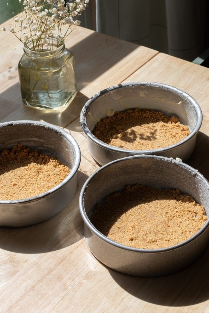 Three 6-inch cake pans with a graham cracker crust at the bottom of them.