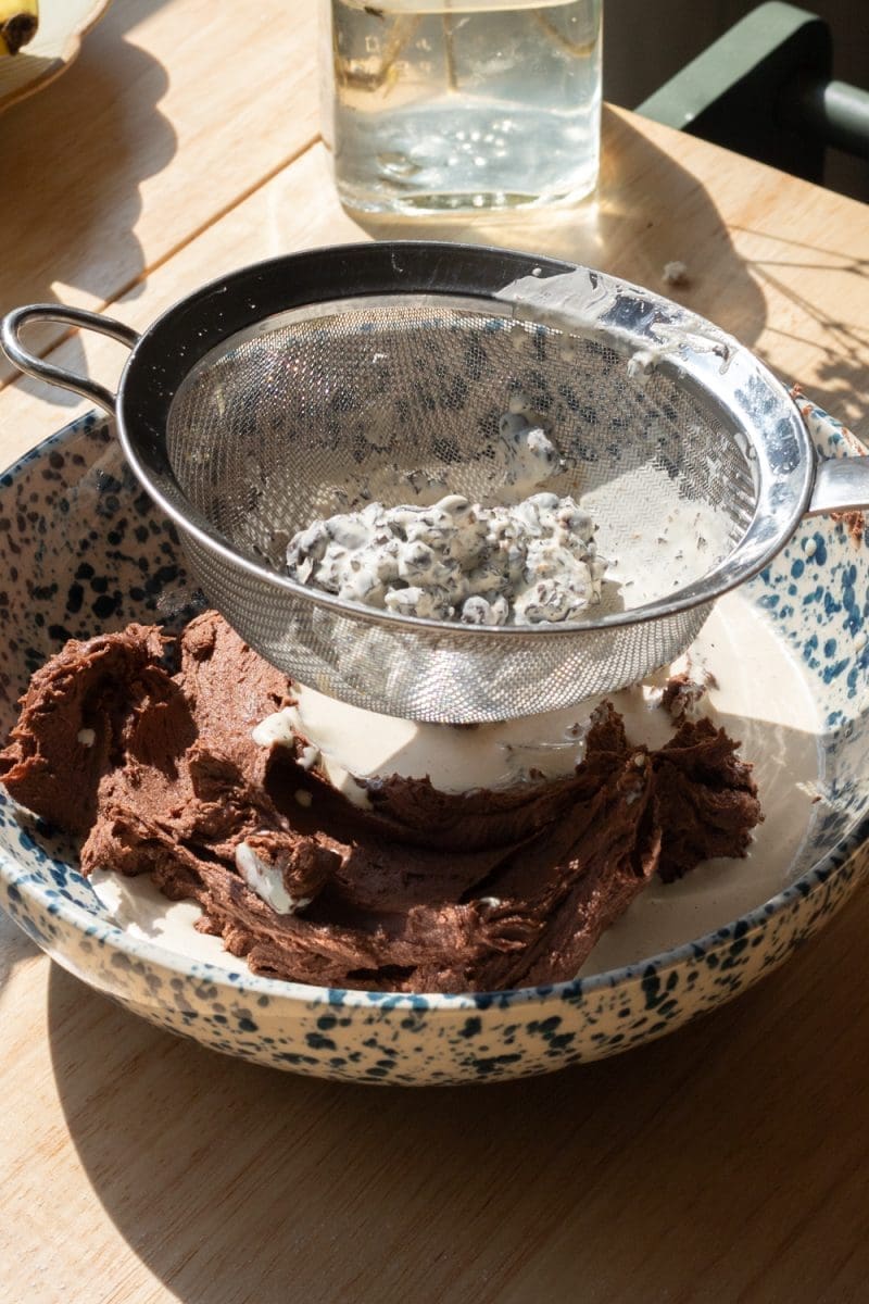 Straining the espresso beans out of the heavy cream over a bowl of chocolate buttercream.