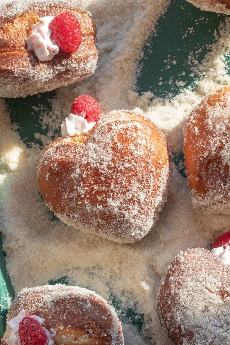 Close up of a filled raspberry cheesecake heart donut.