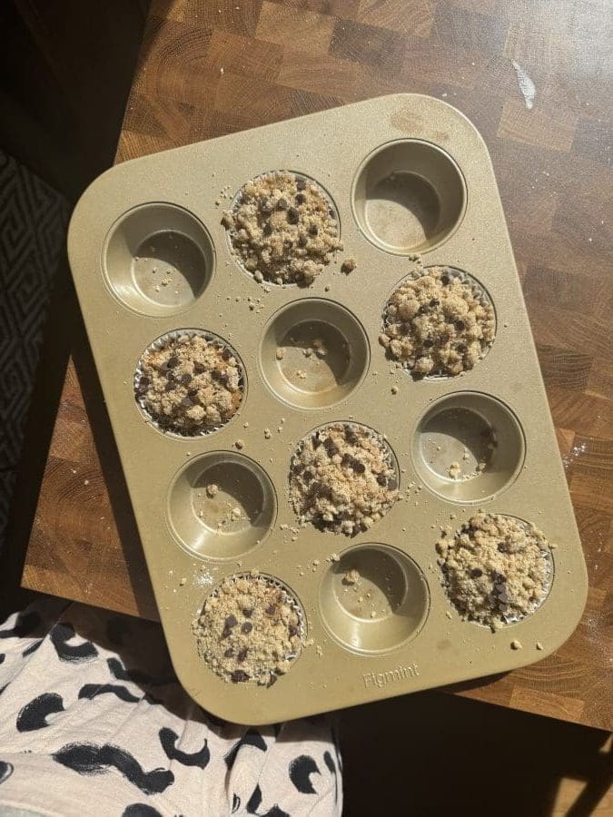 The muffins and streusel distributed in a muffin pan.